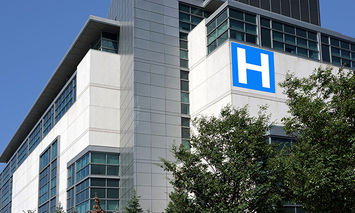 A multi-story hospital building with large windows, displaying a blue 