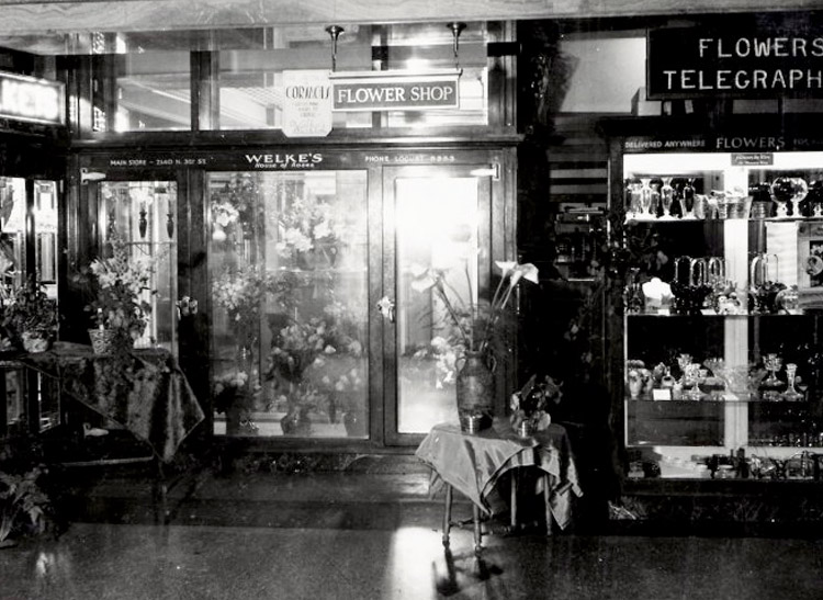 A sign promotes flowers and telegraph services near a glass cooler